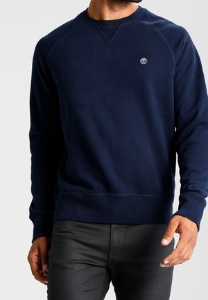 Sweat-shirt bleu marine en tissu doux, avec un col rond et des poignets côtelés. Un petit logo est placé sur la poitrine.