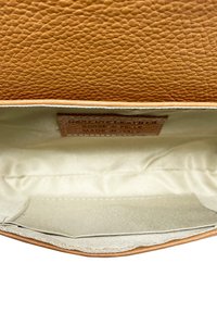 Interno della borsa in pelle marrone con texture, foderato in tessuto crema, tasca laterale, etichetta impressa con istruzioni per la cura, design minimalista.