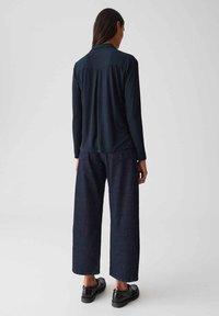 Navy lange mouwen top met een zachte textuur, gecombineerd met een wijde, donkere denim broek. Het schoeisel heeft glanzende zwarte accenten.