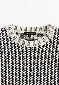 Marineblå og cremefarvet strikket sweater med et struktureret zigzag-mønster, der har en ribbet halsudskæring og et mærke med brandnavnet.