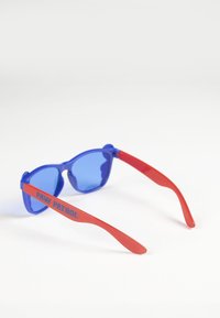 Lunettes de soleil en plastique bleu avec une forme rétro. Les branches rouges comportent le texte "PAW PATROL". Les verres sont légèrement teintés pour protéger des UV.