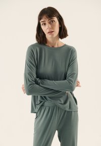 Grünes Langarmoberteil mit lässigem Schnitt und rundem Ausschnitt, kombiniert mit passenden elastischen Hosen mit seitlichen Taschen. Glatte Textur.