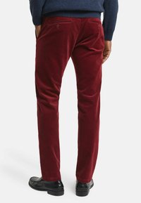 Bordeaux corduroy broek met een rechte snit, voorzien van achterzakken met knopen en een gestructureerd oppervlak. Gemaakt in combinatie met zwarte nette schoenen.