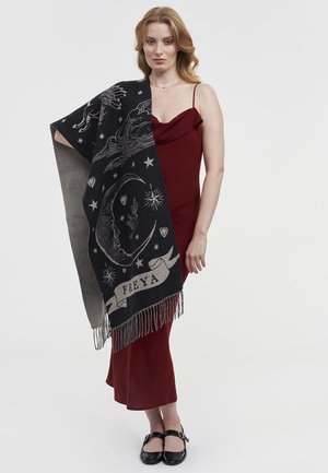 Crni pleteni šal s sivim nebeskim uzorcima, uključujući mjesec, zvijezde i ime "FREYA." Završava se resicama. Model nosi crvenu haljinu.