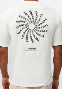 Krem t-skjorte med spiral tekstdesign i svart som leser "DIN TUR" på baksiden, med et mindre slagord nederst. Laget av bomull.
