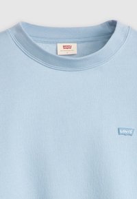 Sweatshirt Levi's bleu clair avec un col rond, des poignets côtelés et un petit patch logo sur la poitrine gauche. Tissu doux et texturé.