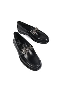 Czarne skórzane mokasyny z zaokrąglonym noskiem, metalowymi łańcuszkami oraz przeszyciami wzdłuż cholewki i podeszwy.