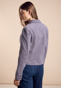 Grå kordjacka med krage, långa ärmar och knappade manschetter; texturerad yta; figurnära design; visad från en sidovinkel.