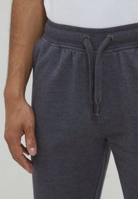 Dark gray joggers made of soft fabric with an elastic waistband, drawstring, and metal accents, showing a relaxed fit and minimal texture.