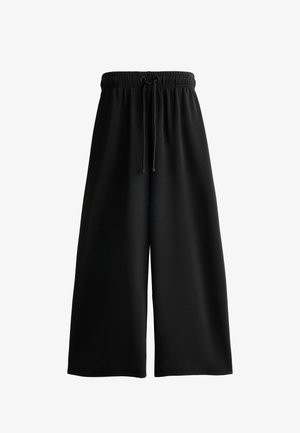 Czarne, szerokie spodnie ścięte w kostkach z elastycznym paskiem w talii i sznurkiem do regulacji. Wykonane z gładkiego materiału o miękkiej teksturze. Bez wzorów i akcentów.