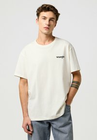 Krémová krátkorpá rukávová tričko vyrobené z bavlny, s malým čiernym logom "Wrangler" na ľavej hrudi. Priamy strih s kruhovým výstrihom.