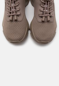 Paire de chaussures de sport couleur taupe avec dessus en tissu mesh et lacets élastiques bungee, vues de dessus sur fond blanc.