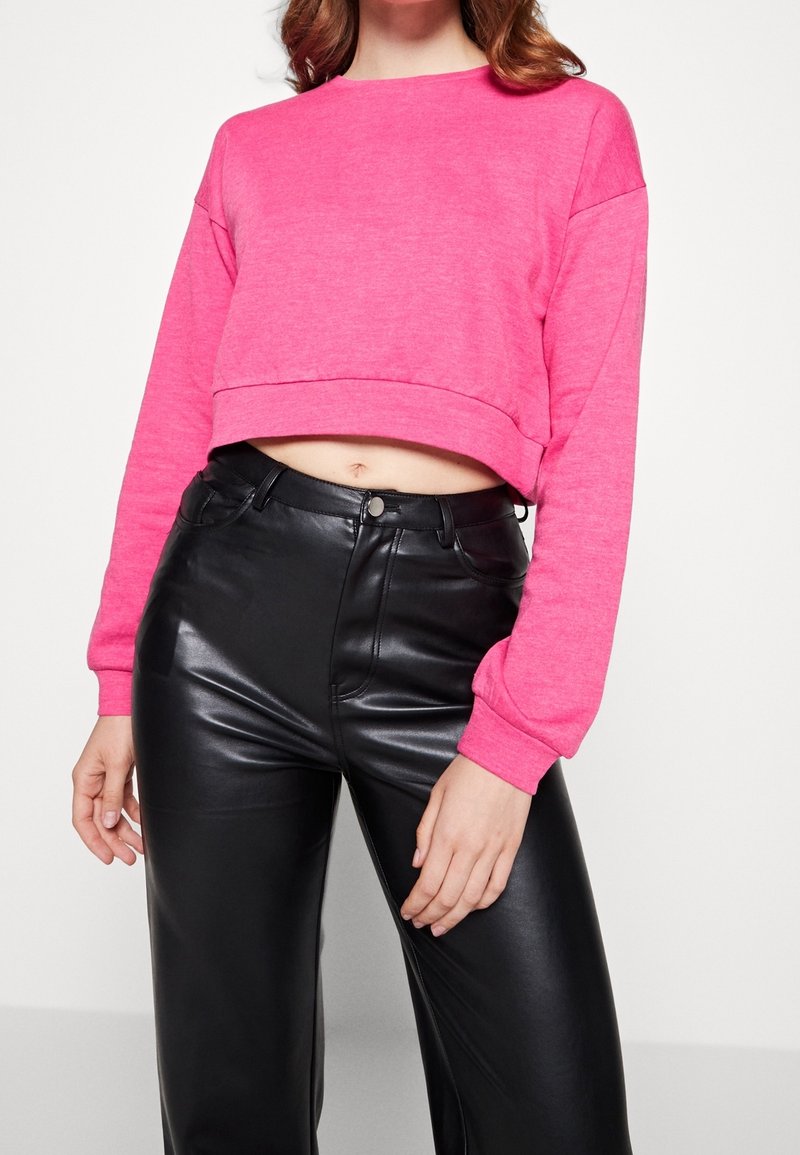 Pink cropped sweatshirt with long sleeves, round neckline, and stretch fabric, paired with high-waisted black faux leather pants.