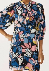 Robe à motif floral noire, avec des nuances de rose, bleu et jaune ; manches bouffantes longues et détail de col à nœud.