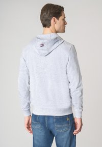 Felpa grigia con tessuto testurizzato, dotata di tasca a marsupio e un piccolo etichetta con logo sul retro. Abbinata a jeans blu.