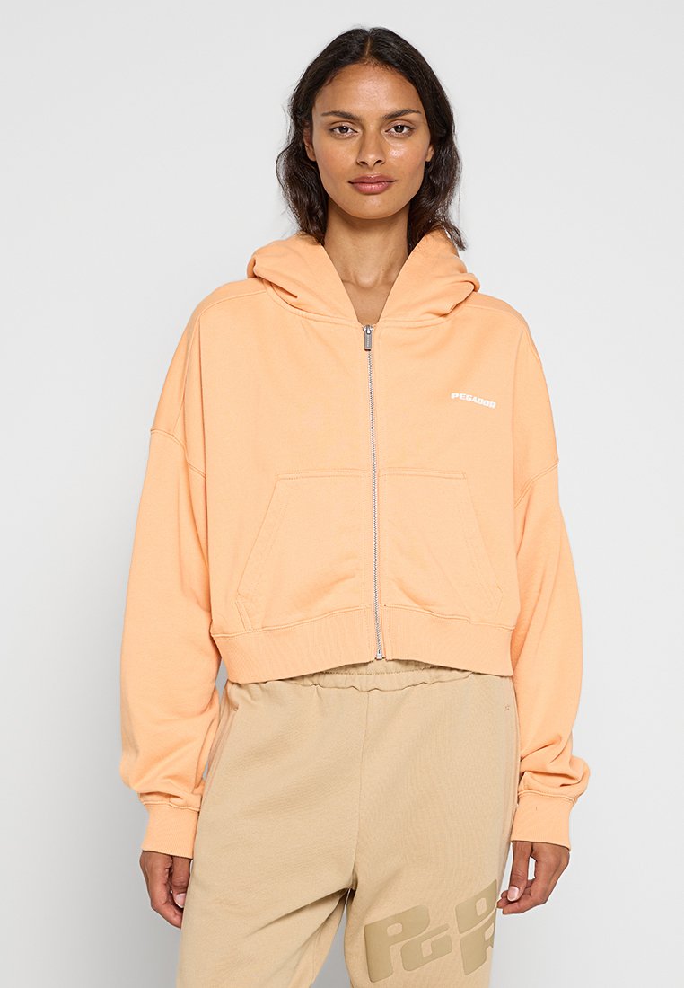 Gekürzte Zip-Hoodie aus weichem Pfirsichstoff mit Kapuze, Fronttaschen und weißen Logodetails. Lange Ärmel mit gerippten Bündchen.