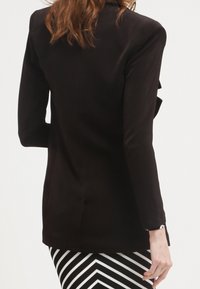 Blazer noir avec une coupe ajustée, doté de manches longues et d'une fente au dos. Assorti à une jupe rayée noir et blanc.