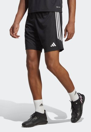 Black athletic shorts with white three-stripe design, paired with black footwear, white ankle socks, and a black athletic top.