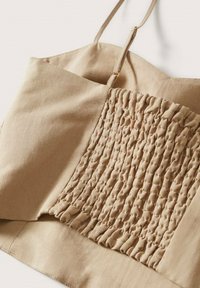 Camisole beige en tissu lisse avec un panneau central texturé et froncé. Fines bretelles ajustables et bord propre avec ourlet.