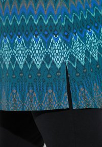 Blaue gemusterte Tunika mit einer Mischung aus geometrischen und abstrakten Designs, seitlichem Schlitz und einer glatten Textur zu schwarzen Leggings.