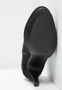 Černá semišová vysoká bota na vysokém podpatku s špičatou špičkou a texturovanou gumovou podrážkou. Viditelné detaily bočního zipu podél svršku.