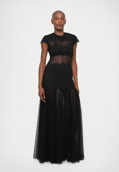 Črna čipkasta obleka z prosojnimi paneli, kratkimi valovitimi rokavi in tekočo krilo. Z vso površinsko čipkastim detajlom in plastenim tilom.