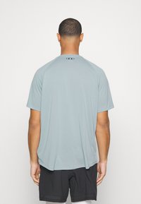 Ljusblå träningströja med kort ärm och rund hals, med raglanärmar, prydd med en svart logotyp på ryggen. Slät tygkvalitet.