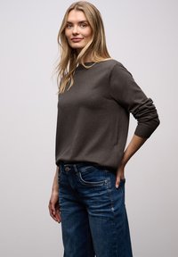 Pull en maille gris foncé avec un col rond et des poignets retroussés, associé à un jean denim bleu avec une conception classique à cinq poches.