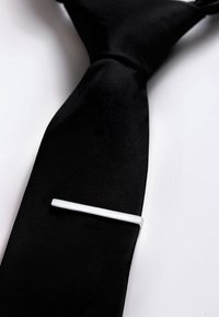 Cravatta in seta nera con una texture liscia, dotata di un fermacravatta in argento, di forma rettangolare, posizionato in diagonale sulla cravatta.