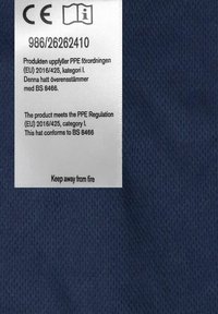 Tummansininen kangas, jossa on kudottu pinta, ja valkoinen huoltotarra. Tarrassa on huolto-ohjeet ja paloturvallisuushälytys useilla kielillä.