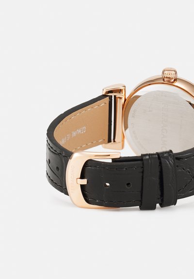 Črni usnjen pašček za uro z zaponko v zlati barvi in okroglim ohišjem ure, na zaponki in notranji strani paščka je prikazana znamka Ferragamo.