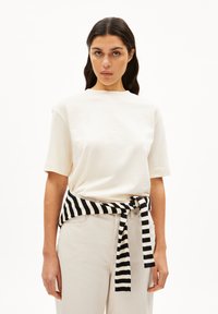 Crème katoenen t-shirt met korte mouwen; gestyled met een zwart-witte gestreepte trui gestrikt om de taille. Lichtgekleurde broek.