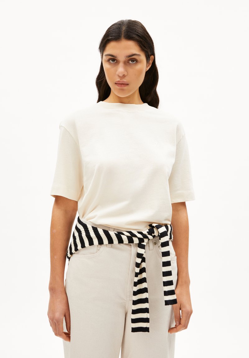 Crème katoenen t-shirt met korte mouwen; gestyled met een zwart-witte gestreepte trui gestrikt om de taille. Lichtgekleurde broek.