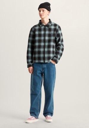 Plaid flannel jacket in black and teal, zippered front, with a collar. Paired with light blue baggy jeans and pink sneakers. Black beanie.