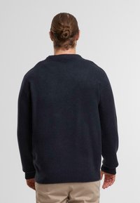 Maglione blu scuro con collo a giro, maniche lunghe, polsini e orlo a costine, realizzato in un morbido tessuto texturizzato. Mostrato di spalle.