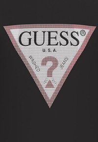 Weißes dreieckiges Logo mit schwarzem Text "GUESS U.S.A." und einem Fragezeichen in der Mitte, umrandet von Rot, auf schwarzem Hintergrund.