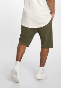 Olijfgroene, getextureerde shorts met een relaxed fit, die net boven de knie eindigen. Gecombineerd met witte sneakers en zichtbare witte sokken.