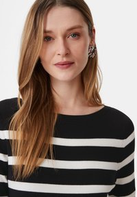 Schwarz-weiß gestreifter Pullover, gerippte Textur, runder Ausschnitt; Modell trägt große, auffällige Ohrringe; langes, glattes Haar.