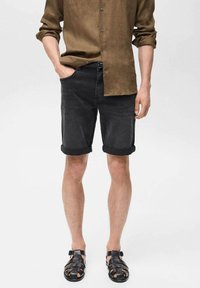 Schwarze Denim-Shorts mit umgeschlagenen Säumen, kombiniert mit einem braunen Leinen-Hemd mit Knöpfen und schwarzen Sandalen, zeigt einen lässigen Look.
