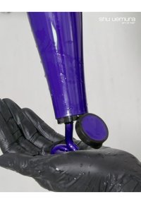 Prodotto per capelli viola in un tubo con compressione, che eroga una formula densa e lucida in una mano guantata nera, posizionato su uno sfondo neutro.