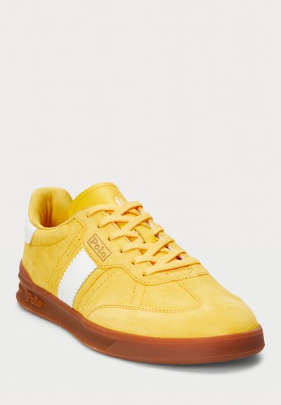Sneaker en daim jaune avec des accents blancs, design à lacets, semelle en caoutchouc et détail de logo sur le côté. Bout arrondi et plat avec une finition texturée.