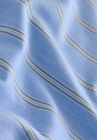 Tissu bleu clair avec un tissage texturé présentant des rayures diagonales crème et bleu marine, présenté en plis doux mettant en valeur sa douceur.