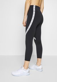 Leggings de sport noirs avec une bande latérale blanche arborant la marque "NIKE". Modèle taille haute, en tissu extensible, silhouette ajustée.