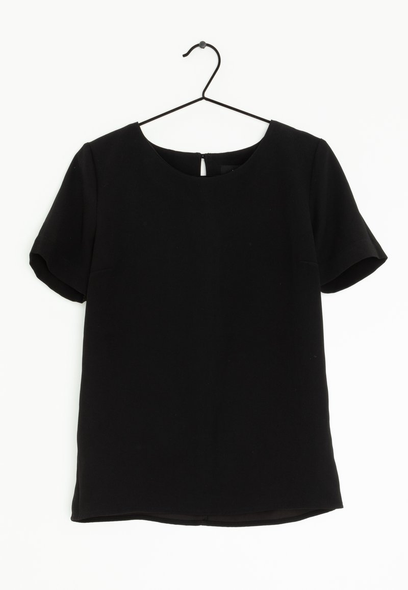 Blusa nera a maniche corte con scollatura tonda appesa a una gruccia in metallo nero su uno sfondo bianco.