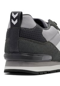 Szary sneaker z materiałów siateczkowych i zamszowych, z fakturowanym tyłem, białymi akcentami oraz warstwową podeszwą z ciemnym obcasem.