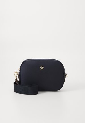 Petit sac bandoulière noir compact avec une large bandoulière réglable et une fermeture dorée, avec un petit logo monogramme doré sur le devant.