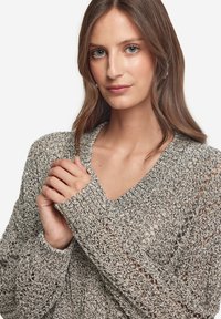 Lätt, stickad tröja i en grå och beige blandning. Har V-ringning, långa ärmar och en strukturerad, öppen vävdesign.