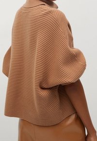Pull en tricot côtelé marron avec un col montant et des manches bouffantes surdimensionnées. Texture douce, coupe décontractée et tissu épais.