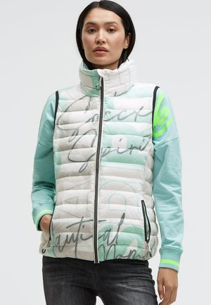 Weiß-grüner, gepolsterter Weste mit hohem Kragen, geometrischem Design und schwarzem Reißverschluss, kombiniert mit einem mintfarbenen Langarmshirt.