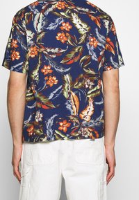Tmavě modrá košile s krátkým rukávem, zdobená tropickým květinovým vzorem s oranžovými květy a zelenými listy, s volným střihem a rovnou lemovkou.